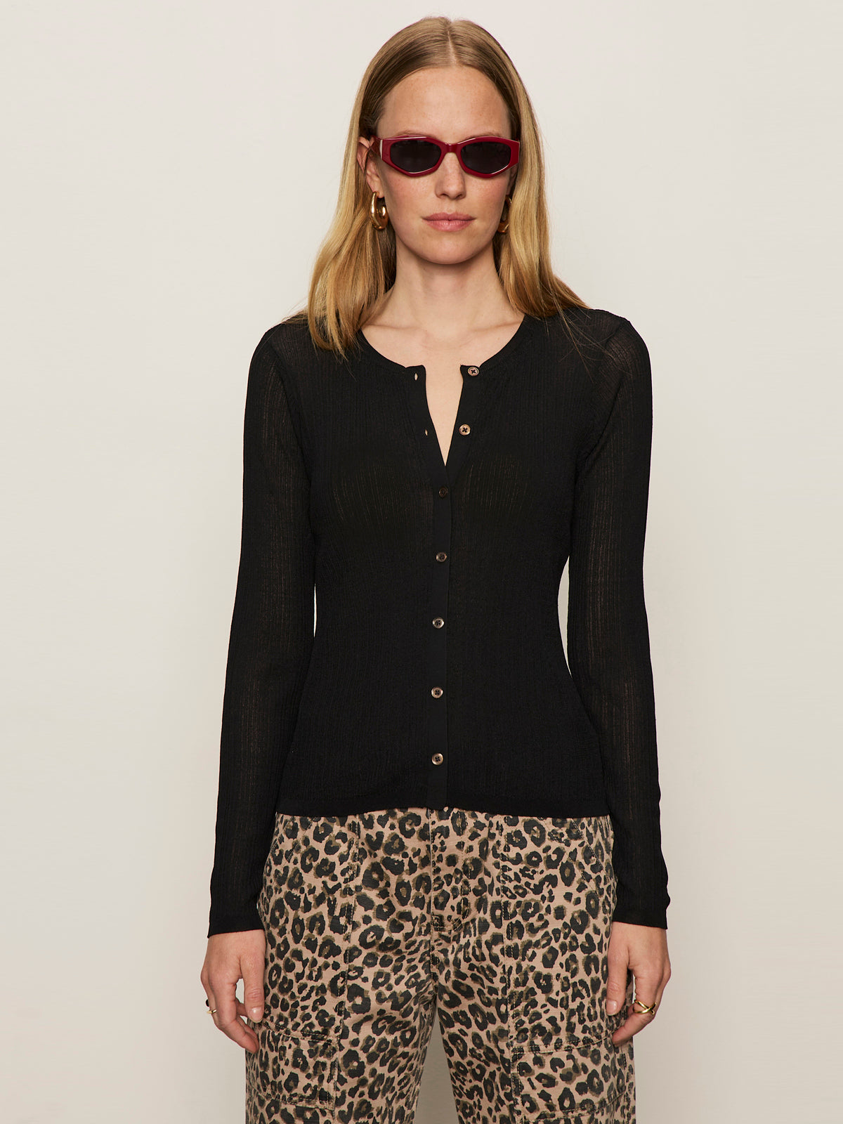 A woman in red sunglasses and leopard print pants models the Sanctuary Clothing lightweight ribbed cardi in black, standing against a plain light background.