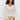 A woman with curly hair wears the Sanctuary Clothing airy openwork sweater macrame in cream and beige pants, standing against a plain white background and looking at the camera with a relaxed expression.