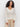 A woman with curly hair wears the Sanctuary Clothing airy openwork sweater macrame in cream and beige pants, standing against a plain white background and looking at the camera with a relaxed expression.
