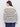 A woman with long dark hair and gold hoop earrings wears the Sanctuary Clothing airy openwork sweater chalk black stripe (extended sizing) and blue jeans, standing with her back to the camera against a plain light background.