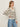 A woman with light brown hair and a neutral expression stands sideways against a plain background, wearing Sanctuary Clothing's airy openwork sweater in chalk black stripe, paired with light blue jeans and gold hoop earrings.
