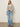 A woman stands against a plain background wearing the Sanctuary Clothing airy openwork sweater in chalk black stripe, paired with light blue high-waisted jeans, black heeled sandals, and gold earrings. Her left hand is in her pocket and she looks relaxed.