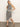 A woman models Sanctuary Clothing's City Summer Tank Black Macrame Stripe 2—a sleeveless black and white striped knit dress with side button accents and an asymmetrical hem—styled with black flip-flops against a plain background.