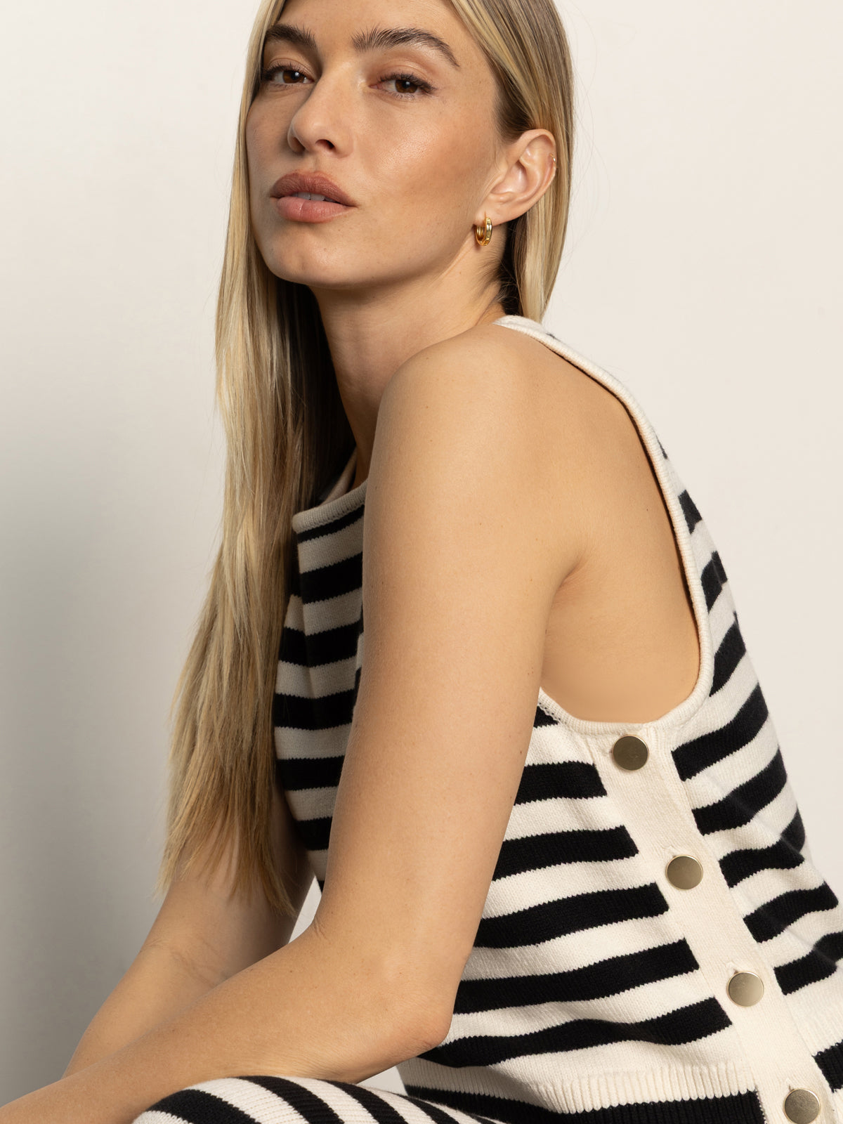 A woman with long blonde hair models the Sanctuary Clothing city summer tank black macrame stripe 2, a sleeveless, black-and-white striped top with side buttons. She gazes confidently at the camera against a plain light background.