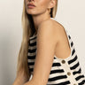 A woman with long blonde hair models the Sanctuary Clothing city summer tank black macrame stripe 2, a sleeveless, black-and-white striped top with side buttons. She gazes confidently at the camera against a plain light background.