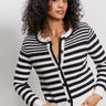 A woman with curly hair models the Sanctuary Clothing city summer cardi in black macrame multi stripe, paired with white pants, standing against a plain light background with her hands in her pockets.