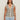 A woman with long brown hair wears the Sanctuary Clothing textured sweater vest macrame black stripe 4, a sleeveless V-neck knit top with black and white stripes, paired with light blue jeans against a plain light background.