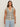 A woman with long brown hair wears the Sanctuary Clothing textured sweater vest macrame black stripe 4, a sleeveless V-neck knit top with black and white stripes, paired with light blue jeans against a plain light background.