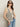 A woman wears Sanctuary Clothing's textured sweater vest macrame black stripe 3 with sunglasses and light blue jeans, posing with one hand in her pocket against a plain light background.