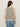 A woman with long brown hair, sunglasses, and blue jeans models the Sanctuary Clothing textured sweater vest macrame black stripe 3, standing with her back to the camera against a plain light background.