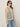 A woman stands in front of a plain light-colored background wearing Sanctuary Clothing's textured sweater vest macrame black stripe 3, sunglasses, and blue jeans.