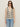 A woman wears the Sanctuary Clothing textured sweater vest macrame black stripe 3, paired with black sunglasses and light blue jeans, standing against a plain light background.