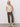 A woman with long blonde hair and a neutral expression models the Sanctuary Clothing textured sweater vest macrame against a plain white wall, styled with olive straight-leg pants and white woven slip-on shoes.