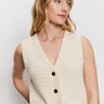 A woman with long, wavy blonde hair models the Sanctuary Clothing textured sweater vest macrame—a sleeveless, cream knit vest with black buttons and front pockets—against a plain white background, looking slightly to the side.