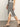 A person wearing the Sanctuary Clothing side slit midi black macrame stripe 2 skirt, paired with a sleeveless top and black flip-flop sandals, walks on a concrete floor.
