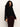 Wearing the Sanctuary Clothing forever cashmere popover in black, a person with long, curly dark hair pairs it with high-waisted dark burgundy pants, standing against a plain light background.
