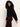 A woman with curly hair looks down while wearing the Sanctuary Clothing forever cashmere popover in black, paired with high-waisted dark red pants, standing against a plain light background.