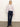 A woman with straight blonde hair and a neutral expression wears the Sanctuary Clothing forever cashmere popover in light twilight mauve, styled with dark blue high-waisted pants and black heeled ankle boots against a plain background.