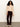 A woman with curly hair wears the Sanctuary Clothing forever cashmere popover in toasted beige, burgundy corduroy pants, and light ankle boots, standing against a white wall and gray floor with a relaxed expression.
