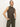 A person with light hair tied back wears the fuzzy shell french kitty sleeveless, high-neck leopard print top from Sanctuary Clothing and olive green pants, standing against a plain white background with hands in pockets.