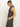 A woman in profile stands against a plain background, wearing Sanctuary Clothing's fuzzy shell french kitty sleeveless leopard print top with high-waisted olive green pants. Her light hair is pulled back in a loose ponytail, and she looks down with one hand in her pocket.