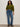 A woman with curly hair wears the Sanctuary Clothing must have cardi in martini olive, high-waisted blue jeans, a leopard-print belt, and black ankle boots. She stands against an off-white wall with one hand in her pocket.