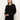 A woman with straight, light brown hair is wearing the Sanctuary Clothing must have cardi black sweater and black pants, standing against an off-white background with a neutral expression.