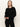 A woman with straight, light brown hair is wearing the Sanctuary Clothing must have cardi black sweater and black pants, standing against an off-white background with a neutral expression.