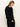 A woman with long, straight light brown hair models the must have cardi black by Sanctuary Clothing, paired with black pants. She stands against a plain light background, looking down and angled to the side.