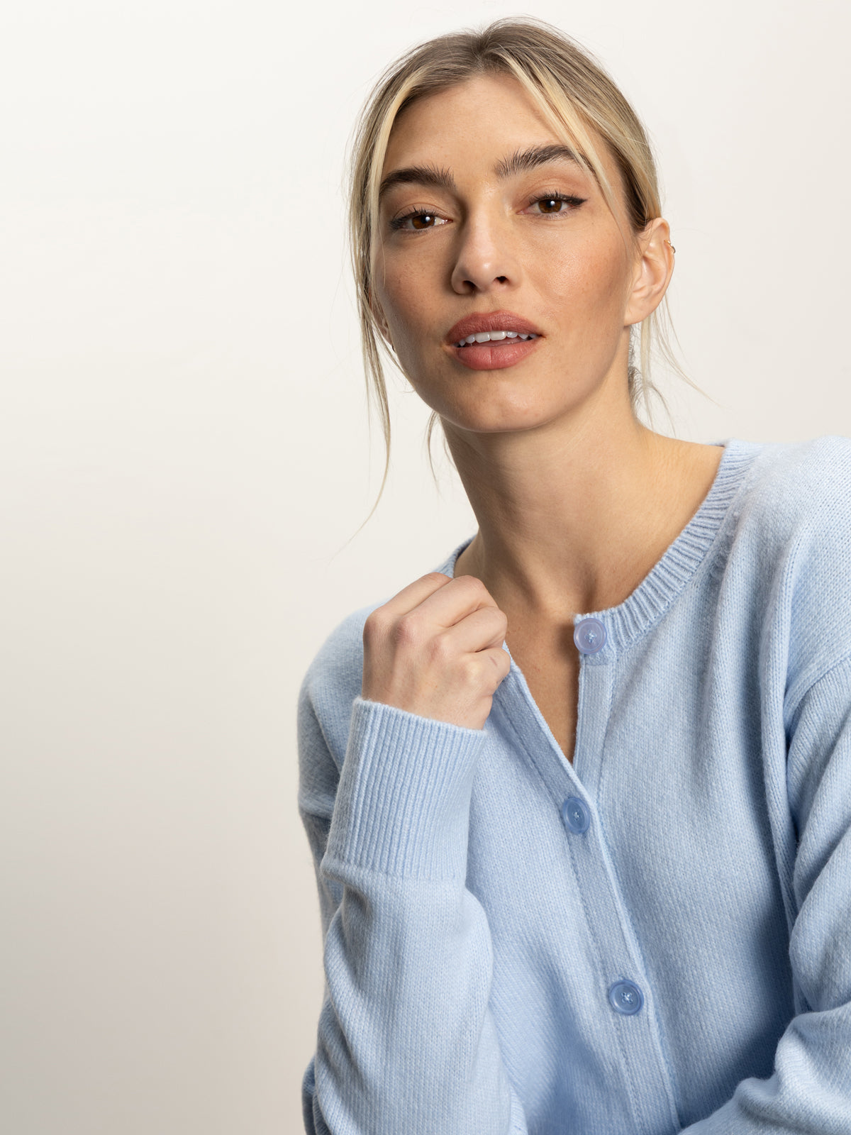 A woman with light hair in a loose ponytail wears the Sanctuary Clothing must have cardi in blue powder, looking at the camera against a plain, softly lit background.