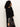 Woman with curly hair wears the Sanctuary Clothing zip it sweater in black and black satin jogger pants with white side stripes, standing sideways against a plain white background.
