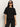 A woman with long dark hair wears black sunglasses and the perfect sweater tee in black by Sanctuary Clothing, paired with black pants, standing against a plain light background.