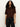A woman with long curly hair wears the Sanctuary Clothing perfect sweater tee in chicory and black pants, standing against a plain light background.