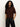 A woman with long, curly hair models the Sanctuary Clothing perfect sweater tee chicory—a short-sleeved, dark brown top—with black leather pants against a light background, hands in her pockets and looking at the camera.
