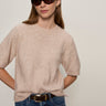 A woman with straight light brown hair and a neutral expression wears Sanctuary Clothing's perfect sweater tee fawn, dark sunglasses, blue jeans with a black belt, standing against a plain light background.