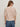 A woman with long, light brown hair wears Sanctuary Clothing's Perfect Sweater Tee in Fawn and blue jeans. She faces away from the camera, highlighting the back of her outfit against a plain light background.