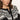 A woman with wavy brown hair wears the Sanctuary Clothing fairisle crewneck cardi in ink multi, featuring a black and white pattern and wooden buttons, as she looks seriously at the camera against a plain background.