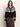 A woman wearing the Sanctuary Clothing fairisle crewneck cardi ink multi, featuring white geometric patterns, pairs it with a dark brown skirt and stands against a light background.