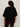 Someone with curly hair is seen from behind, wearing Sanctuary Clothing's ribbed sweater tee in black extended sizing and dark pants, standing against a plain light background.