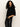 A woman with curly hair models the Sanctuary Clothing ribbed sweater tee in black, paired with black leather pants and posing with one hand in her pocket against a plain, light background.