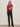 A woman with long hair stands confidently against a plain background wearing the Sanctuary Clothing ribbed sweater tee in cherry lacquer, paired with black leather pants, a patterned belt, and black heeled boots.