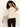 A person with curly hair wears the Sanctuary Clothing ribbed sweater tee in mother of pearl and dark burgundy pants, standing against a plain light background while looking down and touching their hair.