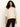 A woman with long curly hair models the Sanctuary Clothing ribbed sweater tee in mother of pearl, featuring wide sleeves, paired with dark burgundy pants against a plain light background.