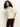 A woman with curly hair wears the Sanctuary Clothing ribbed sweater tee in mother of pearl, paired with burgundy pants, standing against a plain light background.