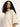 A woman with long, curly dark hair wears the Sanctuary Clothing ribbed sweater tee in mother of pearl, featuring elbow-length sleeves. She stands against a plain, light background and gazes slightly downward with a neutral expression.