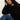 A woman with long curly hair, wearing the Sanctuary Clothing boheme popover black sweater and blue jeans, sits on the floor with one arm on her knee and her head resting on her hand, gazing thoughtfully at the camera.