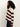 A person with long, curly hair stands sideways against a plain white background, wearing Sanctuary Clothing’s 24 7 popover chicory light oat sweater with dark pants.
