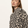 A person with long, straight hair wears the Sanctuary Clothing "soft touch popover spots" sweater in a beige and black leopard print, confidently facing the camera against a plain, light background.