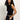 A woman with long curly hair wears the Sanctuary Clothing asymm shoulder twist top in black, styled with dark blue jeans and a leopard print belt, standing against a plain light background.