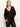 A woman models the Sanctuary Clothing meow cardi kitty camo, a dark brown leopard print cardigan with large buttons, over a black top and black leather pants, standing against a plain background and looking to her left.